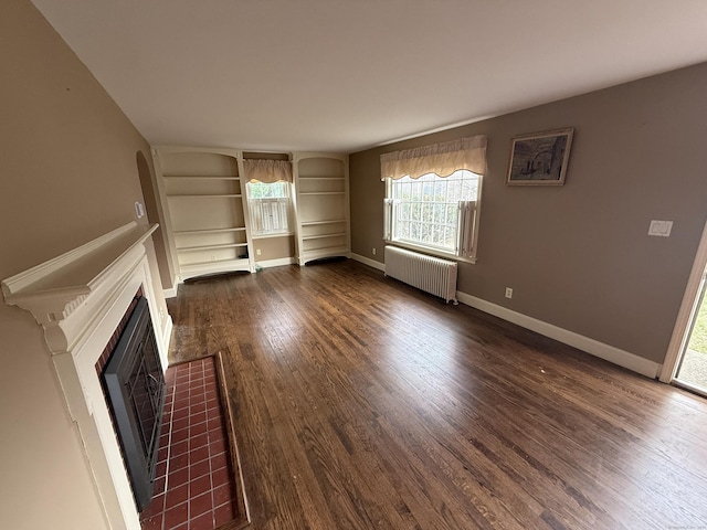 unfurnished living room with radiator heating unit, dark wood-type flooring, baseboards, a fireplace, and built in shelves