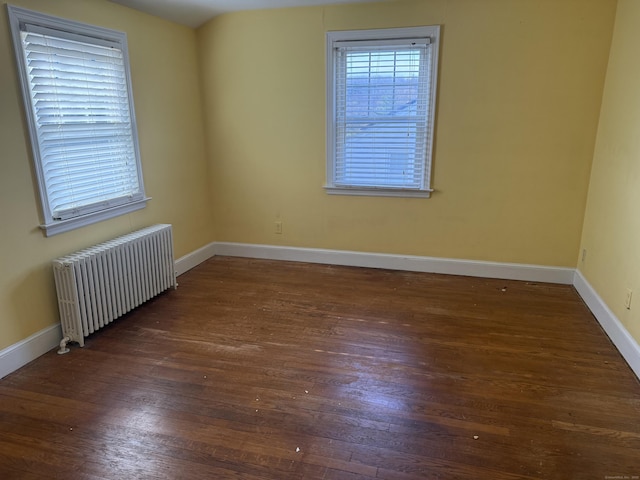 spare room with baseboards, radiator heating unit, and wood finished floors