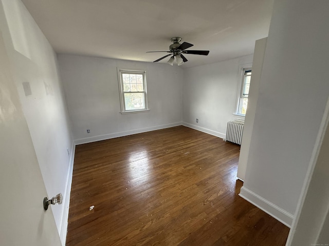 empty room with radiator heating unit, a ceiling fan, baseboards, and dark wood-style flooring