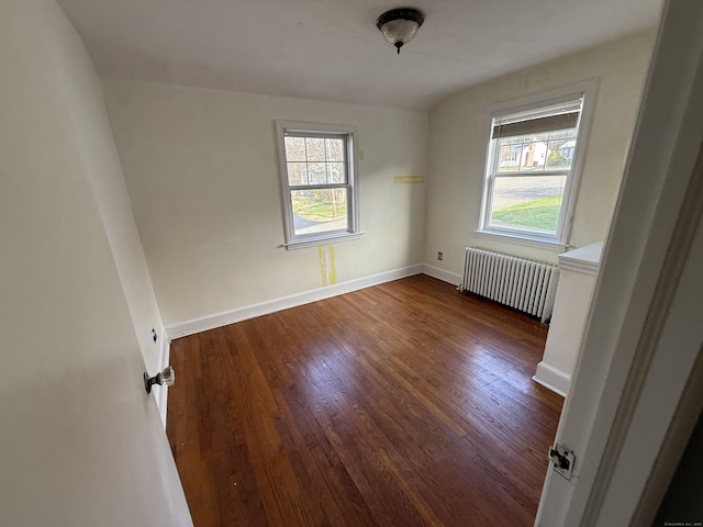 spare room with dark wood finished floors, radiator heating unit, and a healthy amount of sunlight