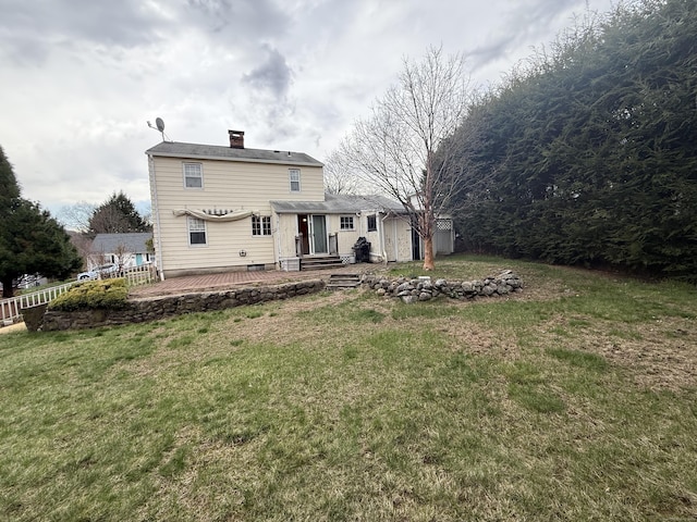 rear view of property featuring a lawn, a chimney, an outdoor structure, fence, and a wooden deck