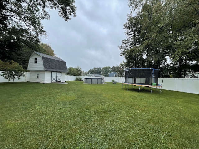 view of yard with a fenced backyard, a trampoline, a shed, and an outbuilding
