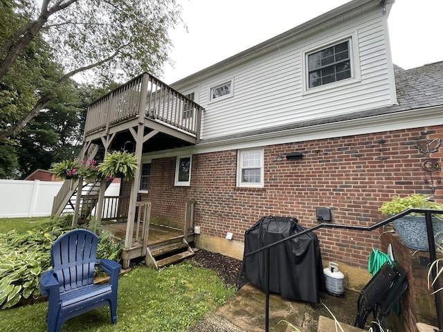 back of house featuring fence, a deck, and brick siding