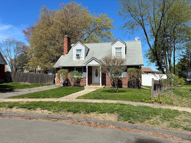 new england style home featuring brick siding, a front lawn, fence, and a chimney