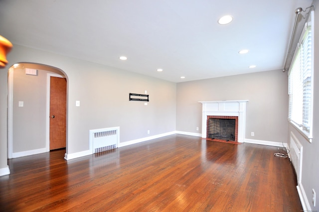 27 Brook St, New Britain, CT 06051 - unfurnished living room with radiator, wood finished floors, arched walkways, a brick fireplace, and recessed lighting