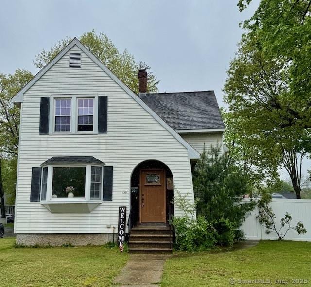 view of front of property featuring roof with shingles, fence, a chimney, and a front yard
