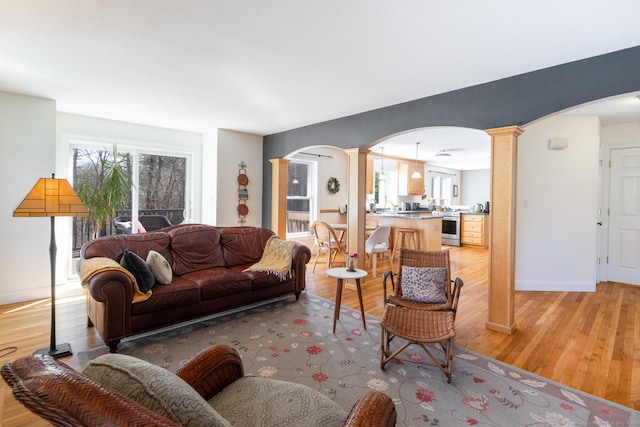 living room with arched walkways, light wood-type flooring, baseboards, and decorative columns