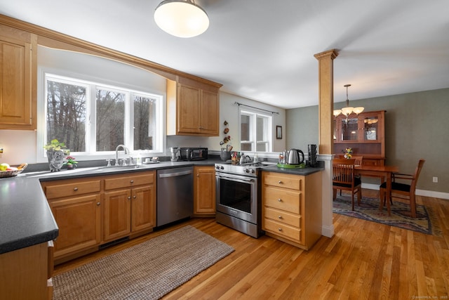 kitchen featuring dark countertops, a sink, light wood-style floors, appliances with stainless steel finishes, and a notable chandelier