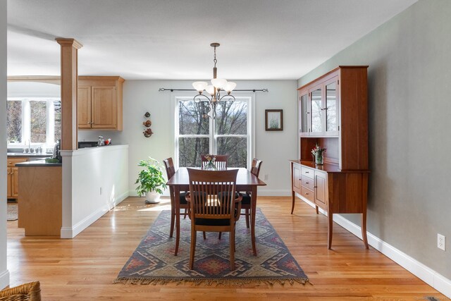 dining area with baseboards, a chandelier, light wood finished floors, and ornate columns