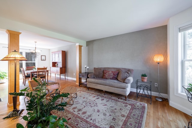 living area featuring baseboards, an inviting chandelier, light wood-style floors, and decorative columns