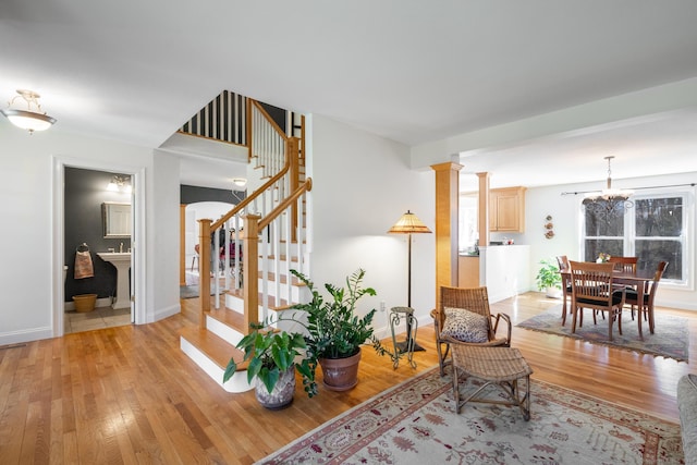 sitting room with ornate columns, light wood-style floors, baseboards, a chandelier, and stairs