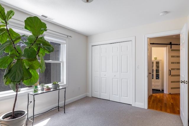 interior space with carpet flooring, a barn door, baseboards, visible vents, and a closet
