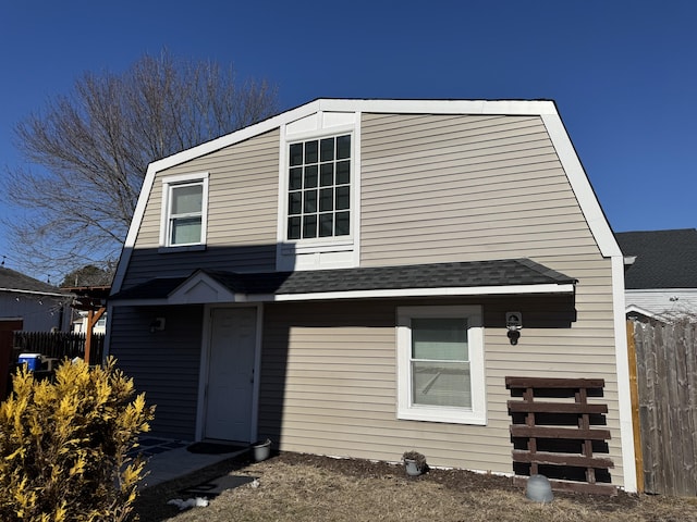 view of front facade with fence, a gambrel roof, and roof with shingles