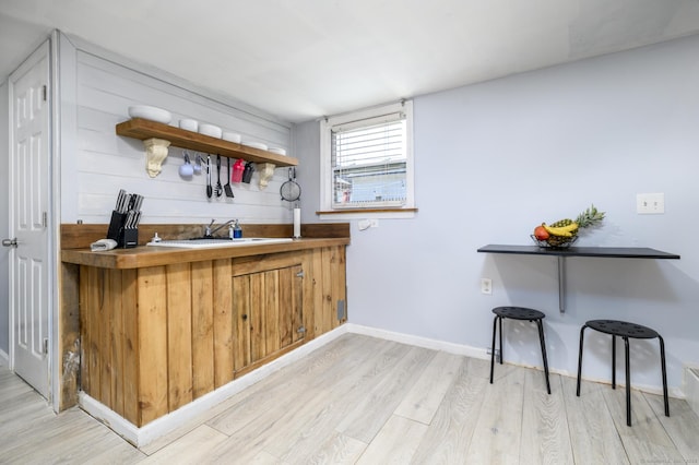 bar featuring baseboards, light wood-style floors, and a sink