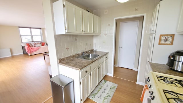 kitchen with a sink, white cabinets, light wood-style flooring, backsplash, and gas range gas stove
