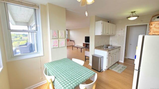 kitchen with white cabinets, freestanding refrigerator, light wood-type flooring, and a sink