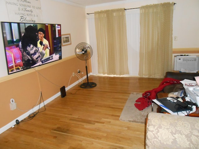 sitting room featuring wood finished floors, baseboards, ornamental molding, and an AC wall unit
