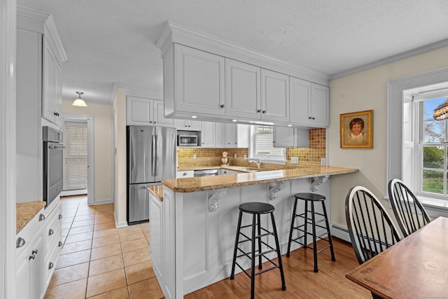9 Academy Ln, Old Lyme, CT 06371 - kitchen featuring appliances with stainless steel finishes, a peninsula, backsplash, white cabinetry, and ornamental molding