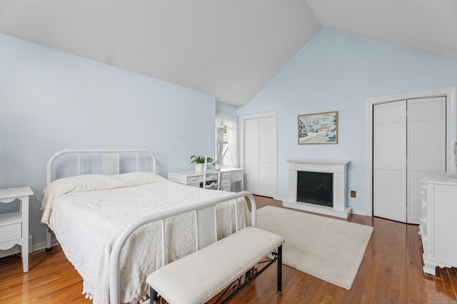 9 Academy Ln, Old Lyme, CT 06371 - bedroom featuring high vaulted ceiling, a fireplace with raised hearth, wood finished floors, and multiple closets