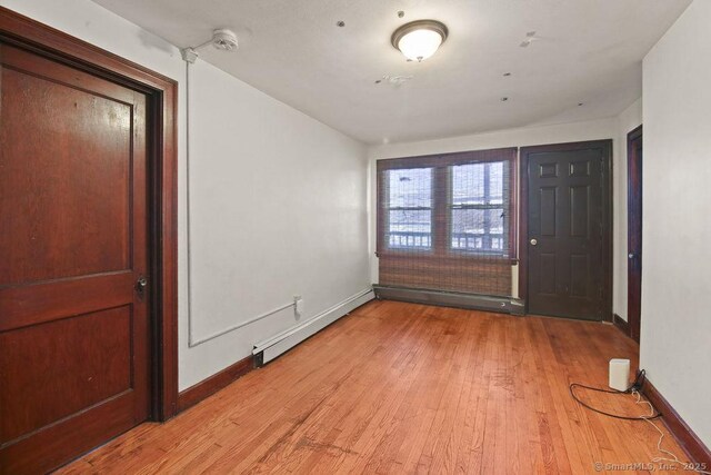 interior space with a baseboard heating unit, baseboards, and light wood-type flooring