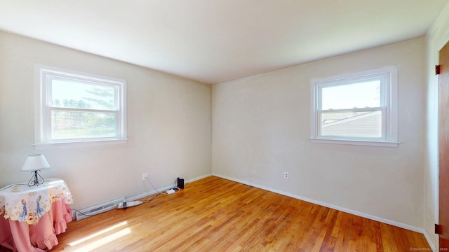 unfurnished room featuring light wood-style floors, a baseboard radiator, baseboards, and a wealth of natural light
