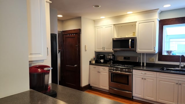 kitchen featuring white cabinetry, dark countertops, appliances with stainless steel finishes, and a sink
