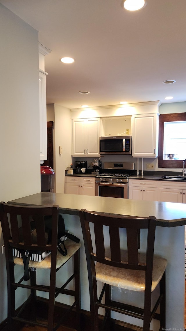 kitchen featuring a breakfast bar area, stainless steel appliances, dark countertops, a sink, and white cabinetry