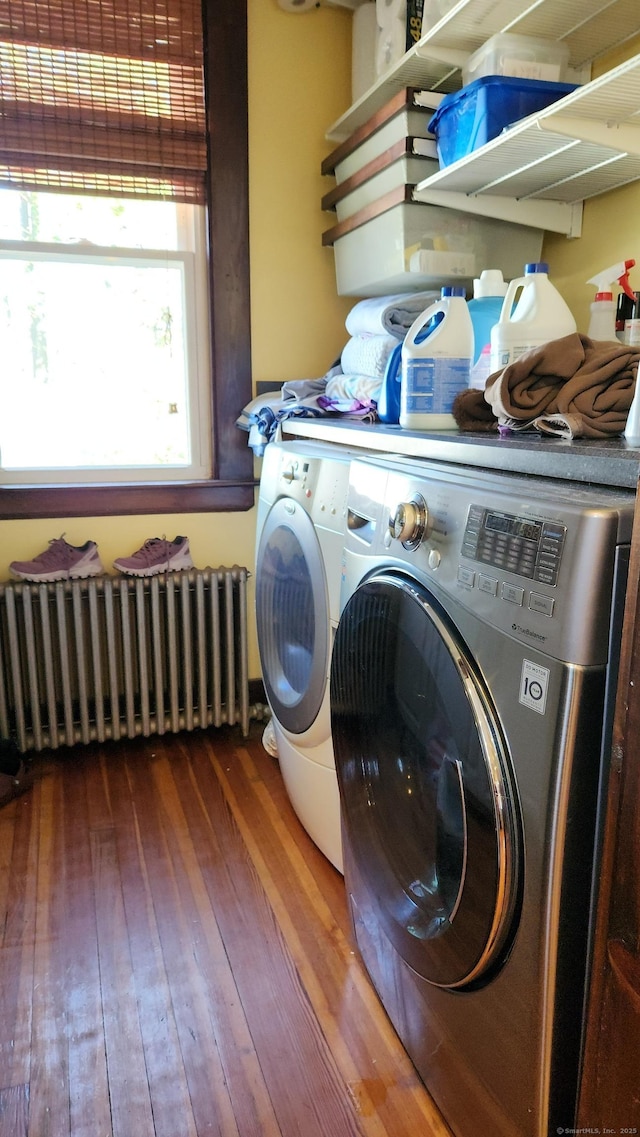 clothes washing area featuring hardwood / wood-style floors, radiator heating unit, washing machine and clothes dryer, and laundry area