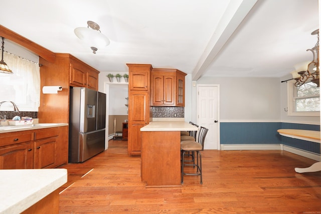 kitchen with a breakfast bar, a sink, light countertops, stainless steel fridge, and brown cabinets