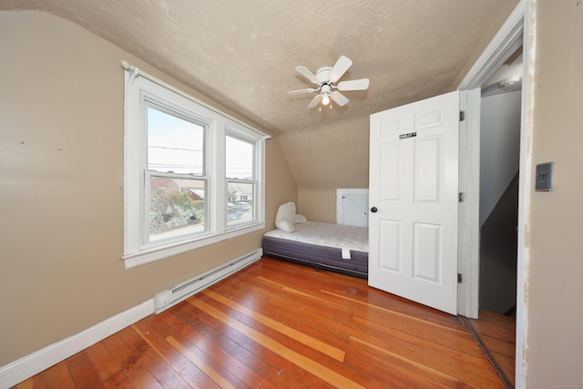bedroom with a textured ceiling, a baseboard heating unit, lofted ceiling, wood-type flooring, and baseboards
