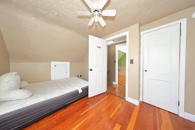 bedroom with a textured ceiling, baseboards, vaulted ceiling, and hardwood / wood-style flooring