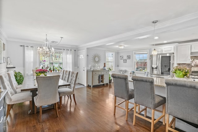 dining area with dark wood finished floors, a chandelier, ornamental molding, and a decorative wall