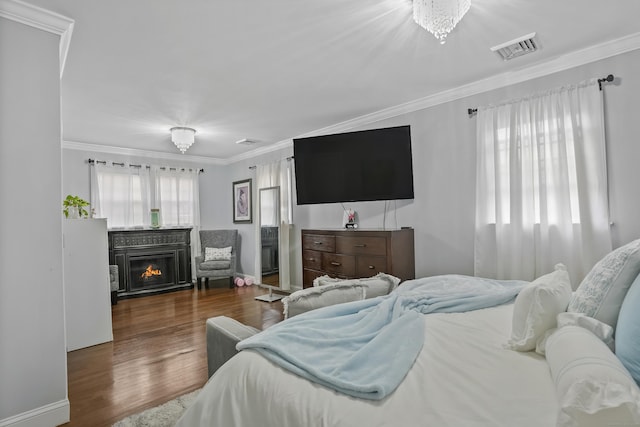 bedroom featuring ornamental molding, a glass covered fireplace, wood finished floors, and visible vents
