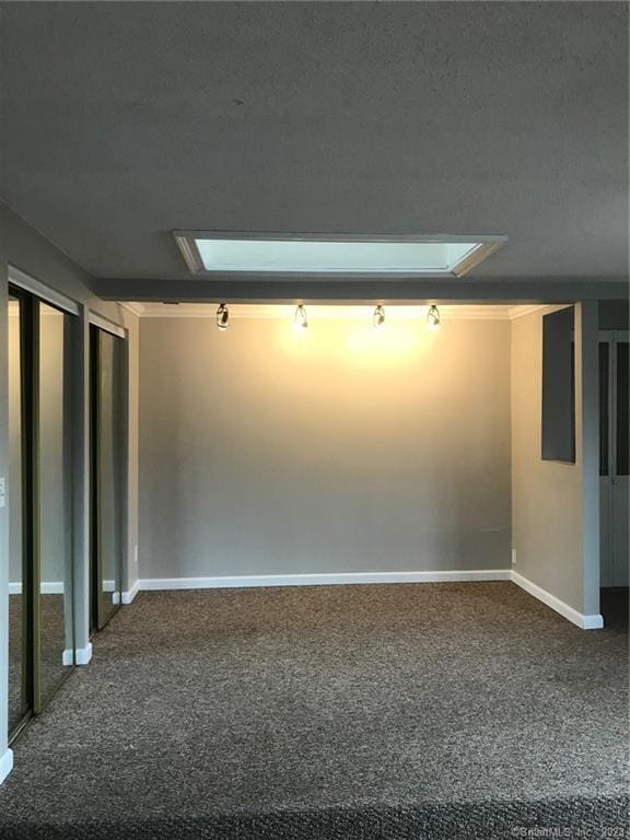 carpeted empty room with attic access and baseboards