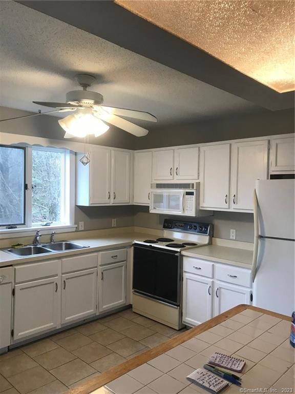 kitchen with white appliances, a textured ceiling, white cabinets, light countertops, and a sink