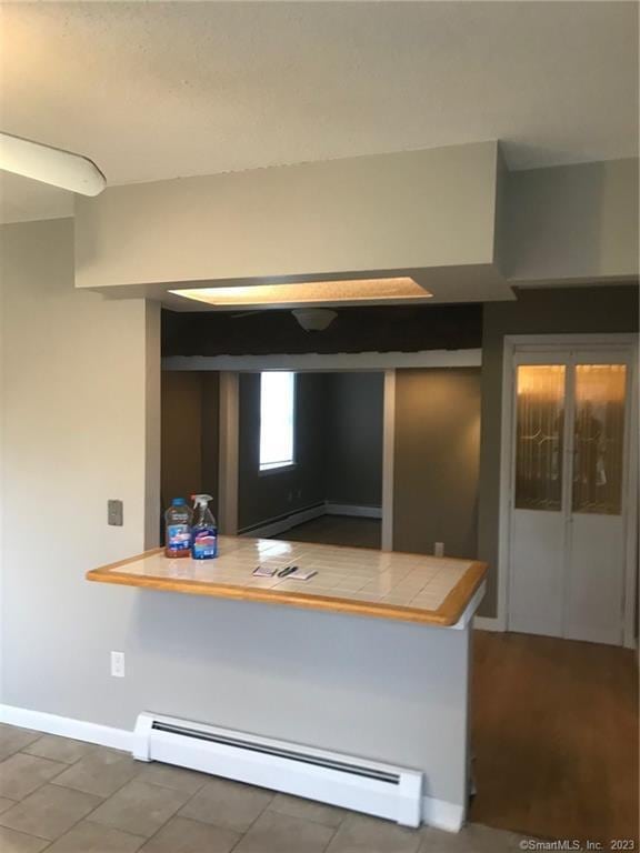 kitchen with tile counters, a baseboard radiator, a peninsula, and baseboards