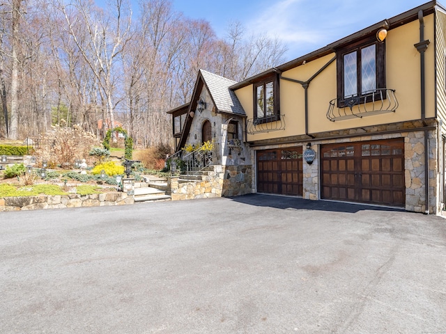 view of property exterior with a garage, driveway, stone siding, and stucco siding
