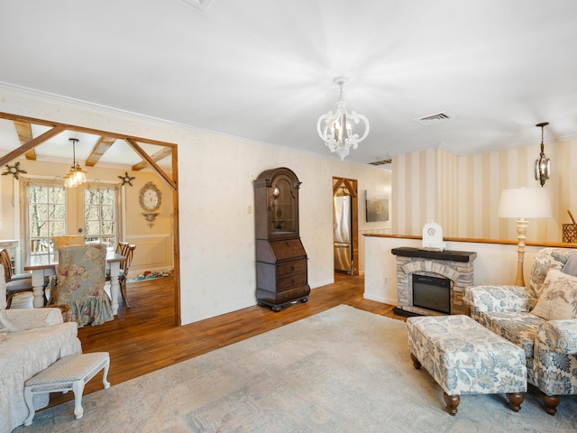 living area with visible vents, a chandelier, wallpapered walls, wood finished floors, and crown molding