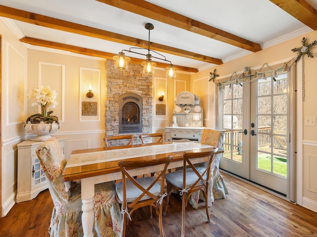 dining room featuring wood finished floors, a stone fireplace, french doors, beamed ceiling, and crown molding