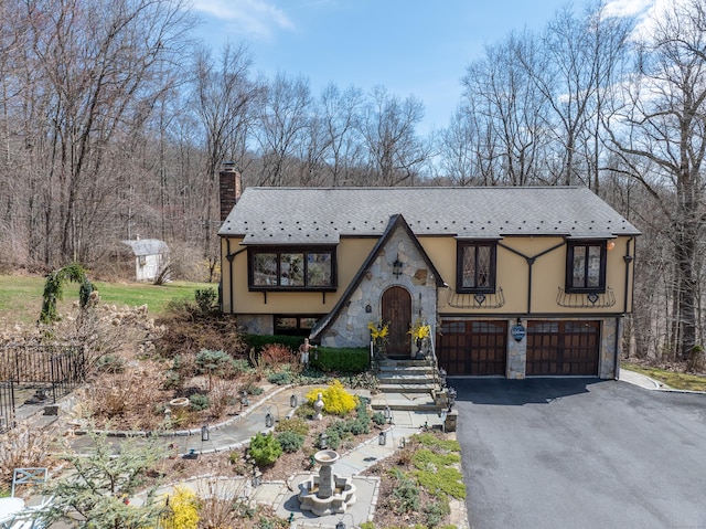 english style home with a chimney, an attached garage, aphalt driveway, and stone siding
