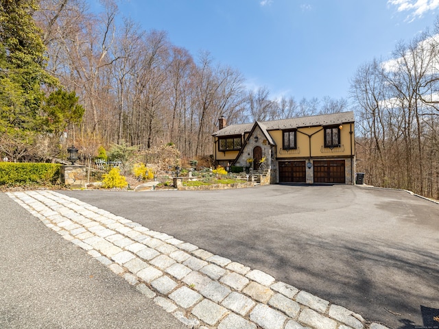 view of front facade featuring a chimney, stucco siding, driveway, stone siding, and a garage