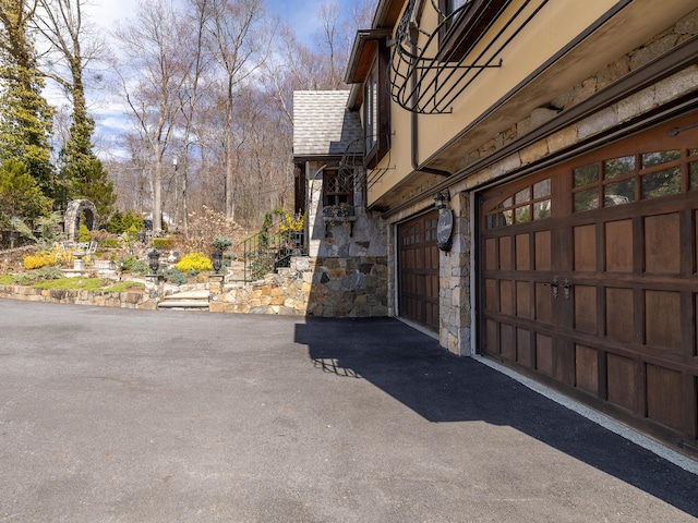 view of side of property featuring aphalt driveway, stone siding, and a garage