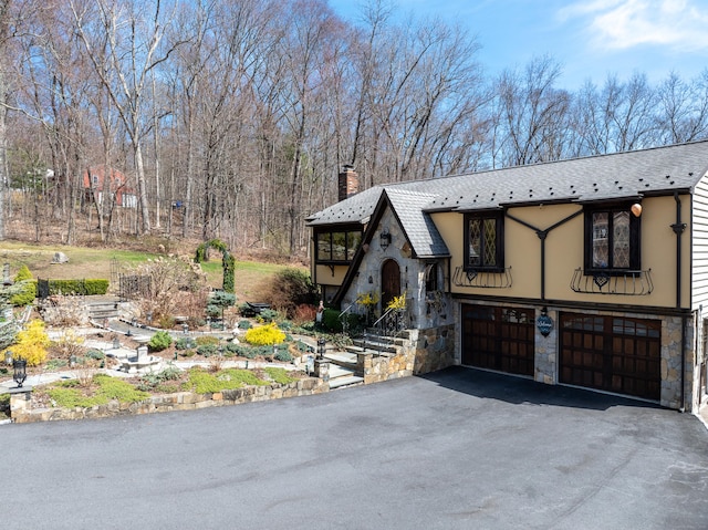 view of front facade with stone siding, driveway, a chimney, and a garage