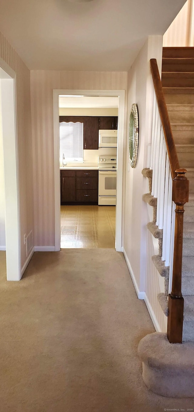 hallway with stairs, baseboards, wallpapered walls, and light carpet