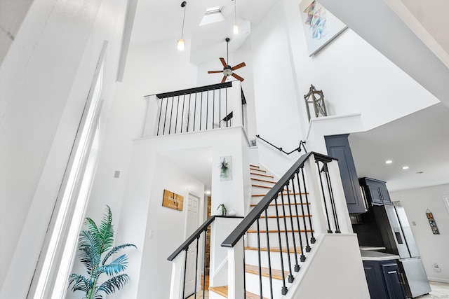 stairs with a skylight, ceiling fan, a towering ceiling, baseboards, and recessed lighting