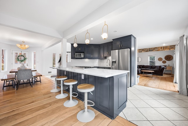kitchen featuring light wood-style flooring, a notable chandelier, a breakfast bar, decorative light fixtures, and appliances with stainless steel finishes
