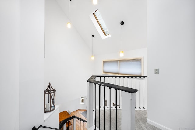 corridor featuring baseboards, a skylight, and high vaulted ceiling