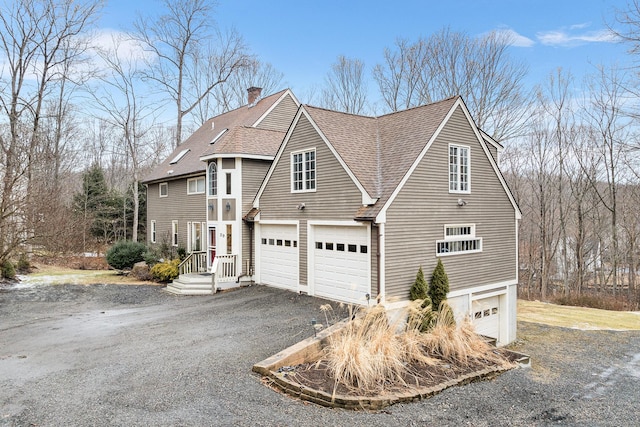 view of side of home featuring a chimney, an attached garage, driveway, and a shingled roof