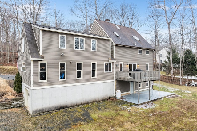 back of house featuring a chimney, a deck, roof with shingles, and a patio