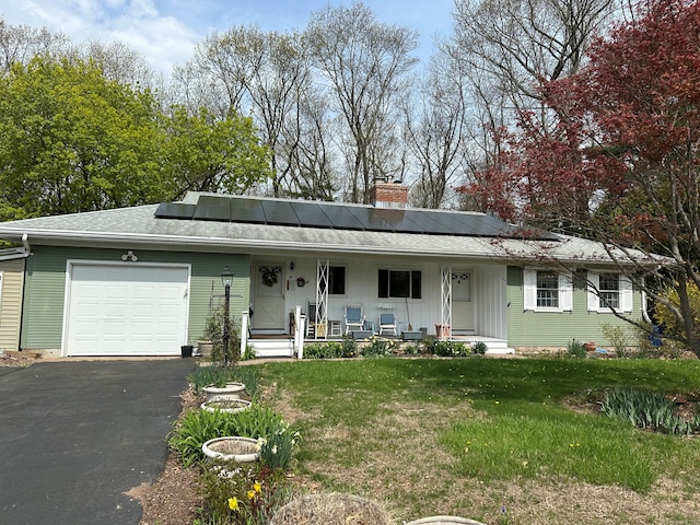 view of front of home with aphalt driveway, a chimney, covered porch, a front yard, and a garage